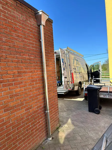 Glanzende zinken regenpijp met vergaarbak tegen een bakstenen gevel – dakwerk door Prodak, Temse