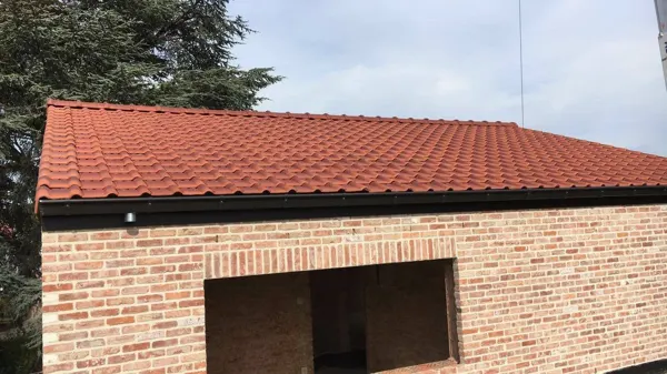 Afgewerkt zadeldak met rode gegolfde pannen en zwarte dakgoot – dakwerk door Prodak, Temse