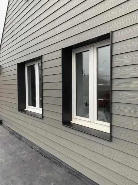 Ramen in een gevel met houtnerf-sidings en zwarte aluminium dagkanten – dakwerk door Prodak, Temse