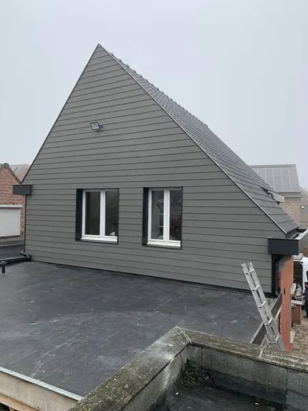 Volledige puntgevel bekleed met grijze sidings boven een plat dak – dakwerk door Prodak, Temse